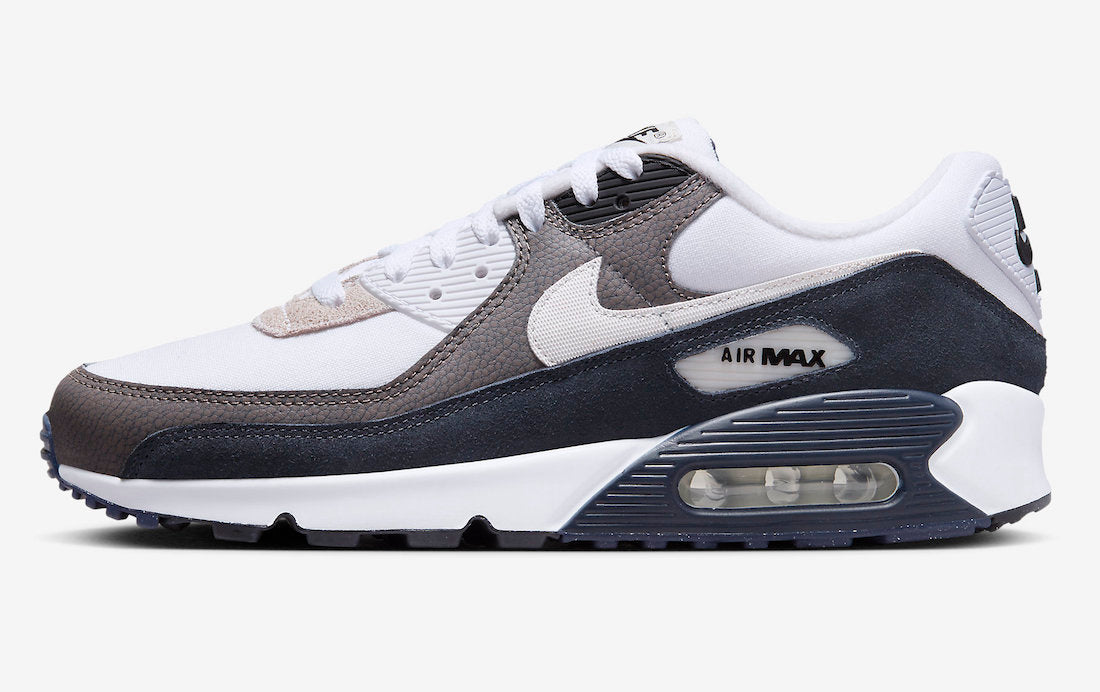 A pair of Nike Air Max 90 sneakers in white, particle grey, black, and volt color, with a mesh upper and a black leather mudguard.