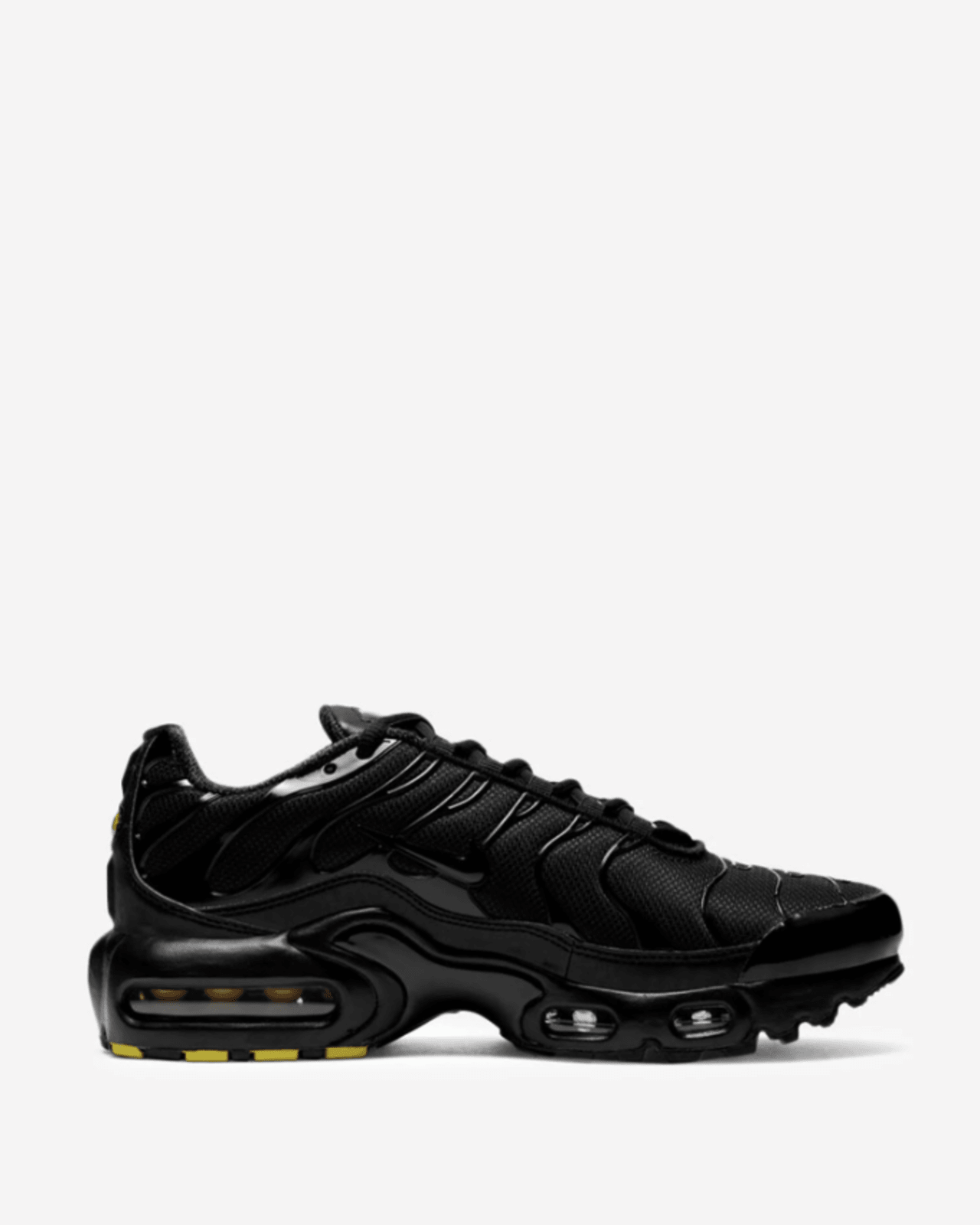 A pair of Nike Air Max Plus Triple Black (GS) sneakers for kids, showcasing the side profile with a all-black color scheme and visible Air Max cushioning units.